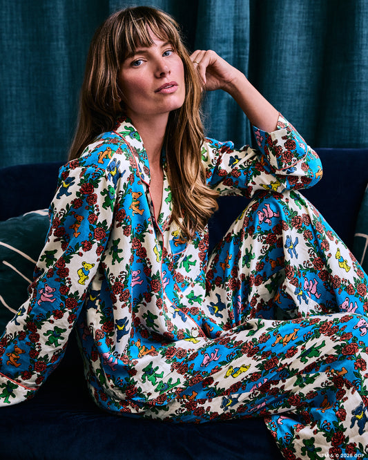 Model seated on a dark sofa wearing a long-sleeved pajama set with a colorful bear-and-rose print.