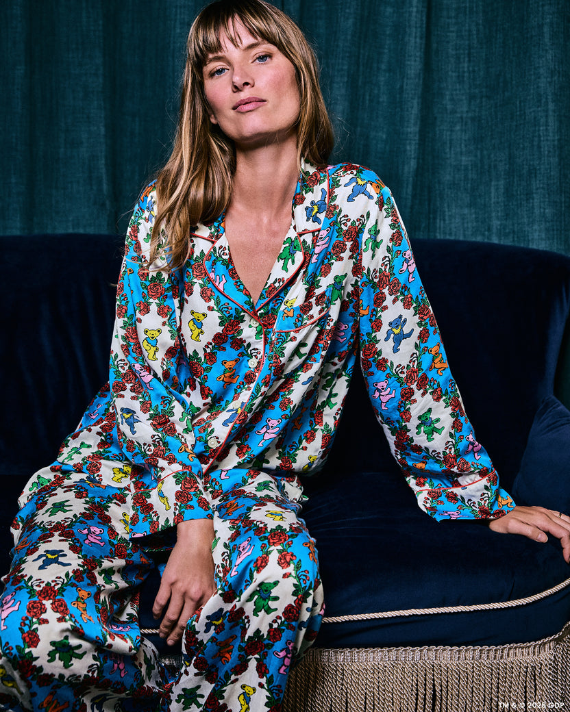 Model seated on a sofa wearing the long-sleeved bear-and-rose print pajama set, shown from the front.