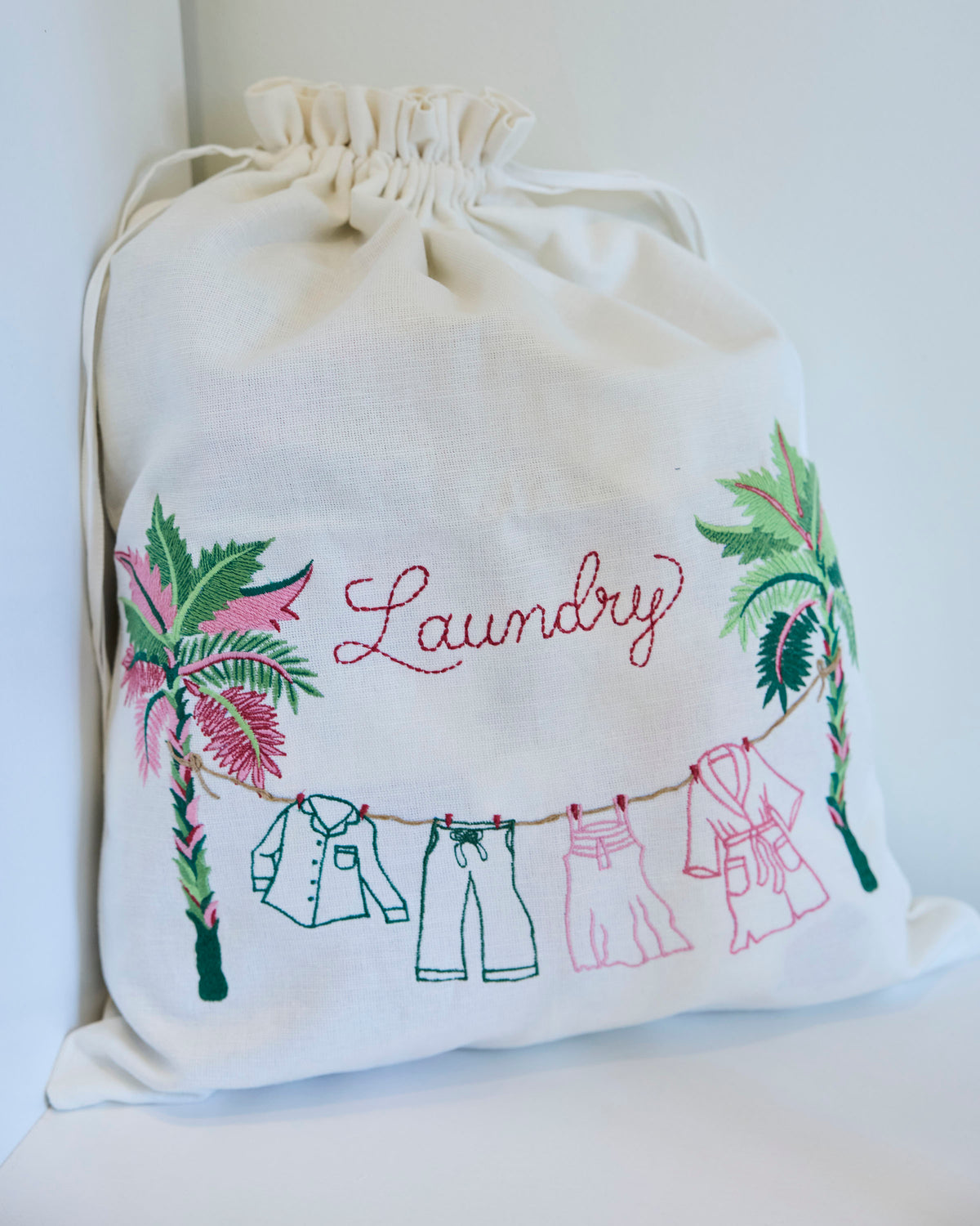 Drawstring laundry bag embroidered with the word “Laundry,” palm leaves, and clothes hanging on a line.