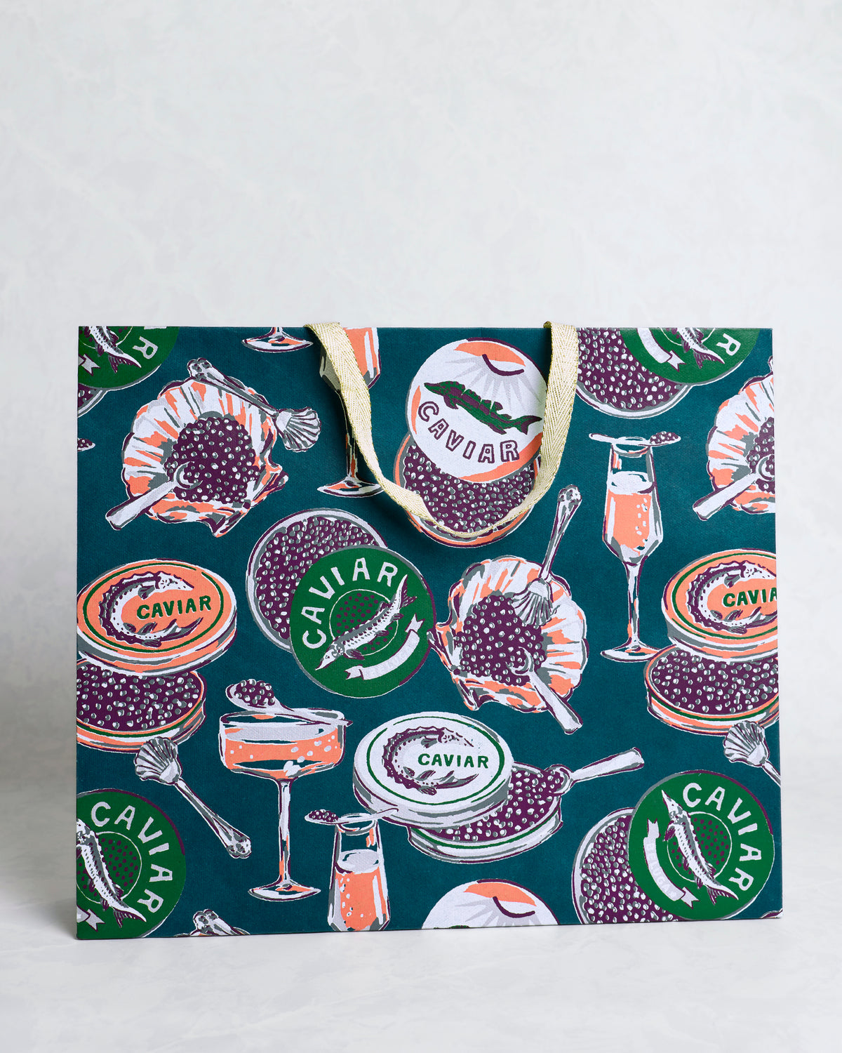 Front view of the Champagne and Caviar peacock feather gift bag with caviar tins, spoons, shells, and champagne glasses on a dark teal background.