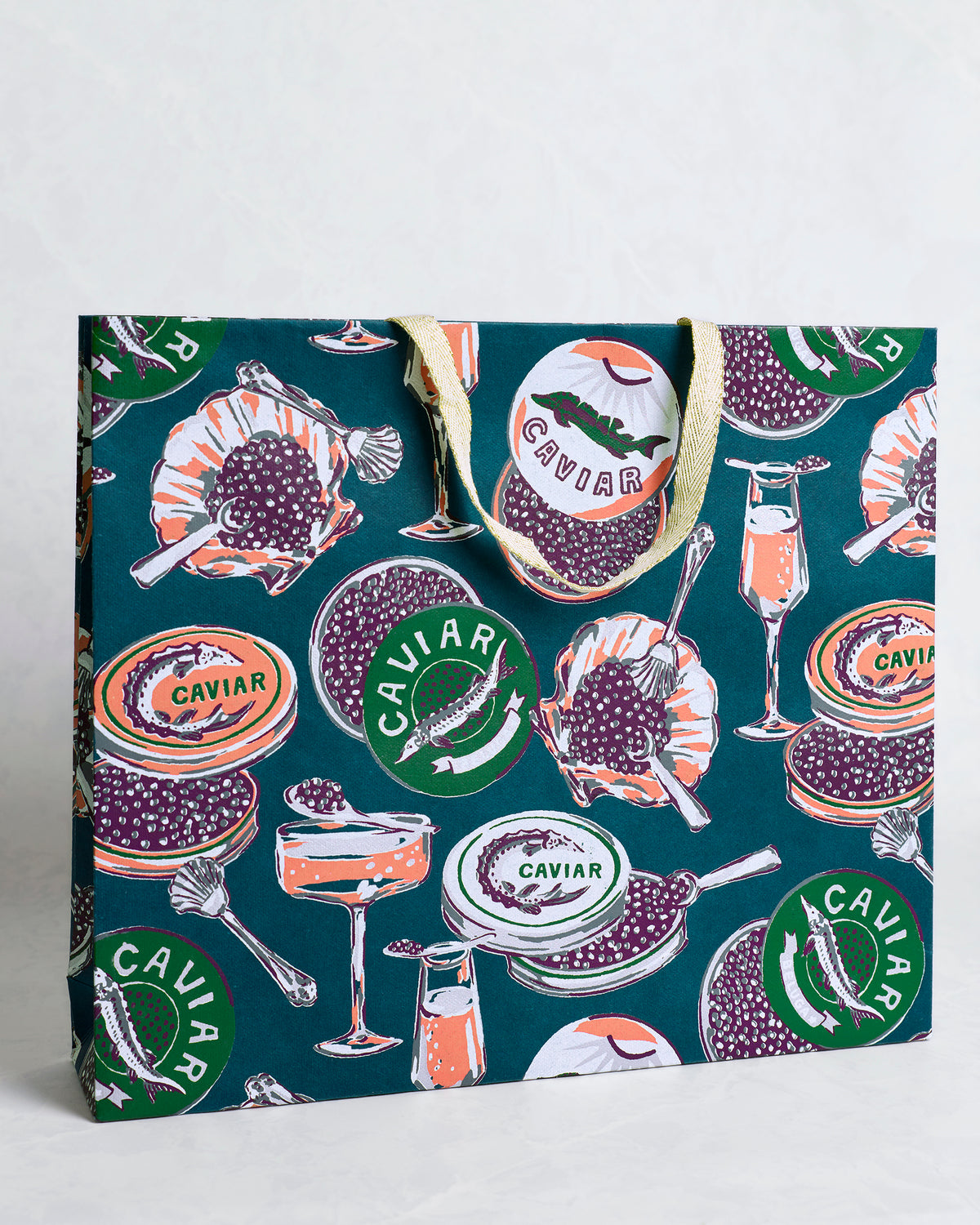 Angled view of the Champagne and Caviar peacock feather gift bag showing its front and side panels with caviar tins, spoons, shells, and champagne glasses.