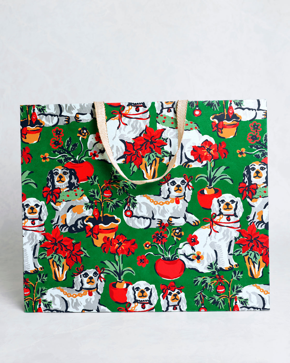 Front view of the Good Dog Christmas evergreen paper gift bag with dogs, poinsettias, ornaments, and tan handles.