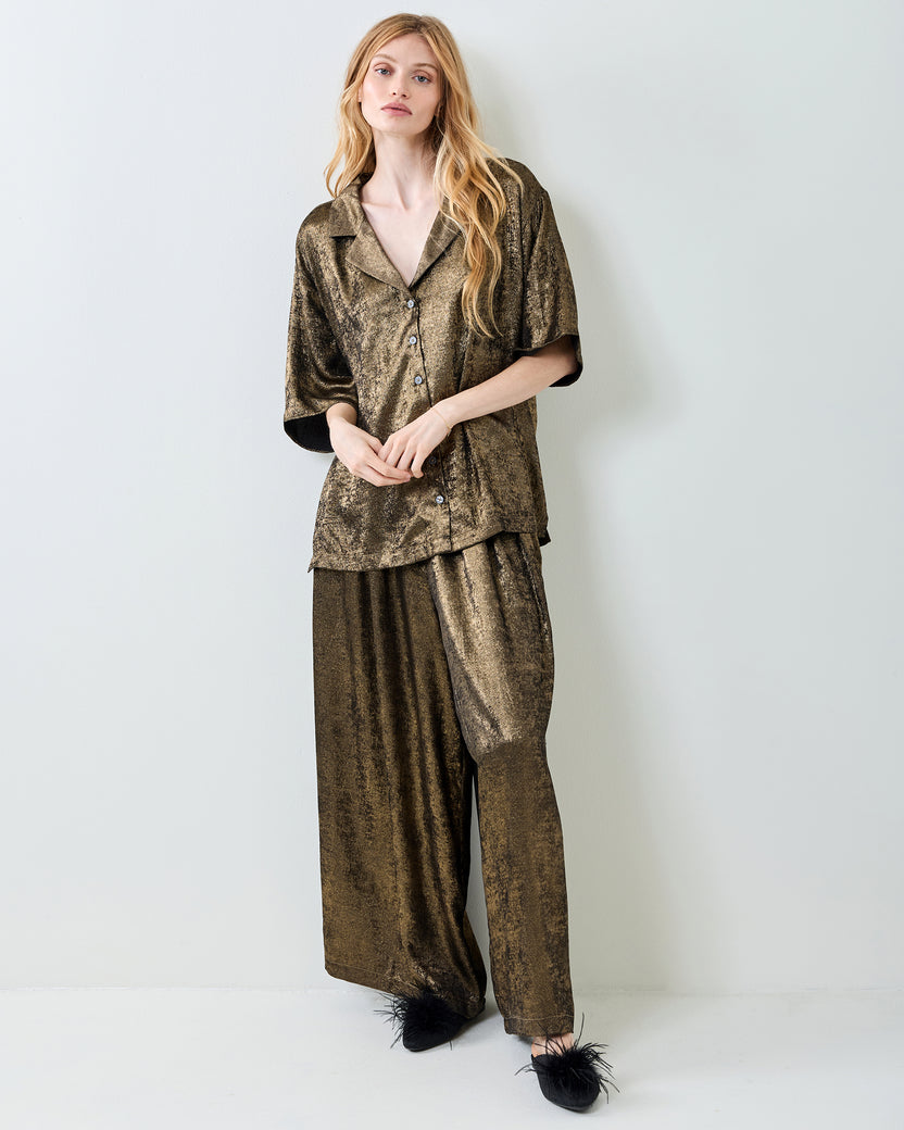 Full-length front view of the gold Blakely pajama set, with a button-down top, wide-leg pants, and black feather-trimmed shoes.