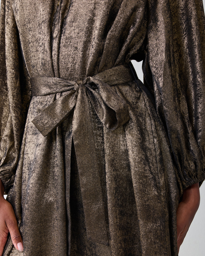 Close-up of the gold Glitzy Lamé Felicity dress showing its waist tie, gathered sleeves, and pockets.
