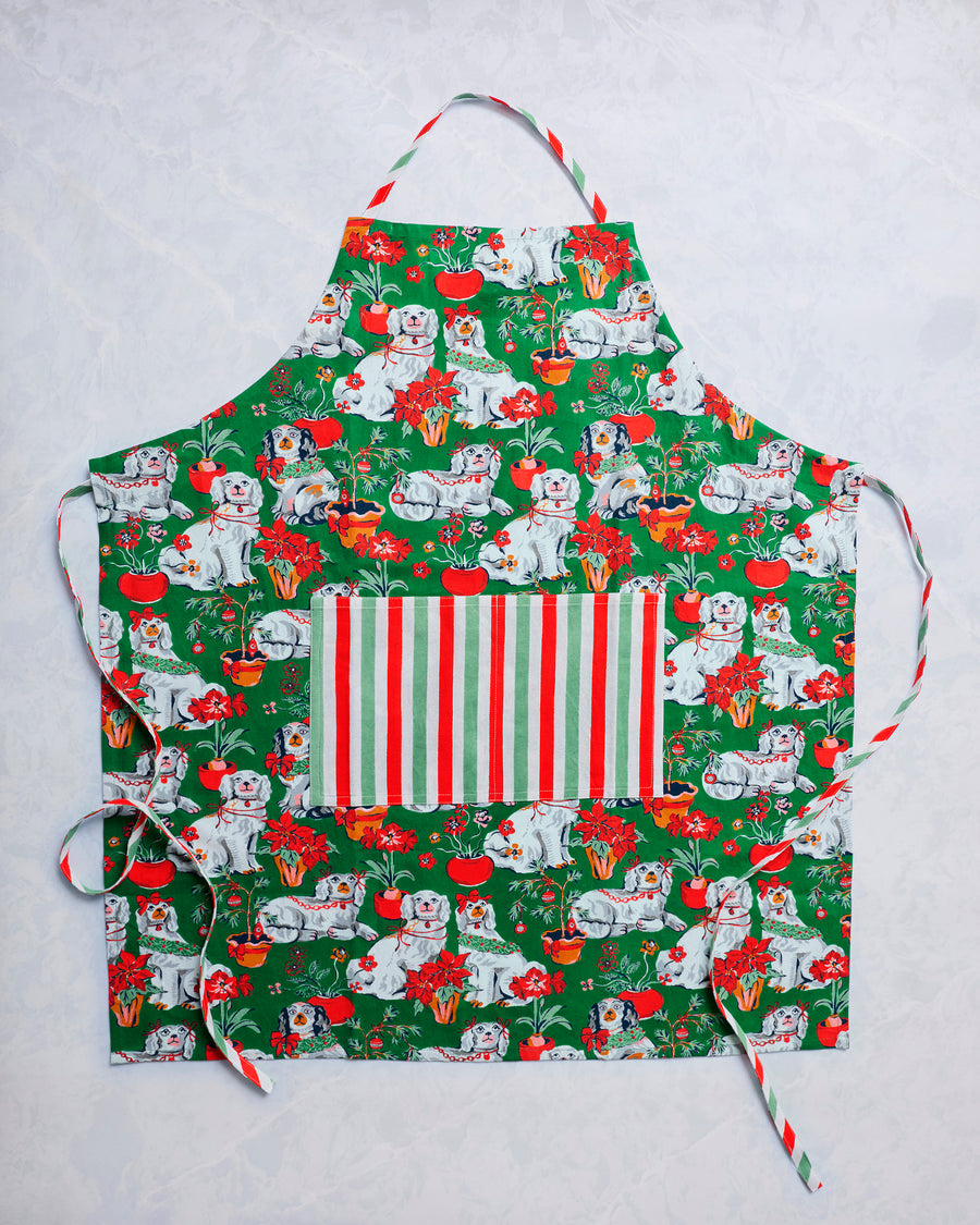 Green Good Dog Christmas apron with an all-over dog and holiday plant print, striped front pocket, and neck strap