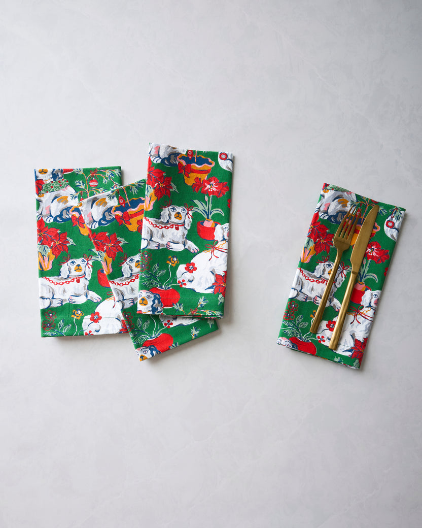 Four green Good Dog Christmas dinner napkins displayed together, with one folded around a fork and knife.