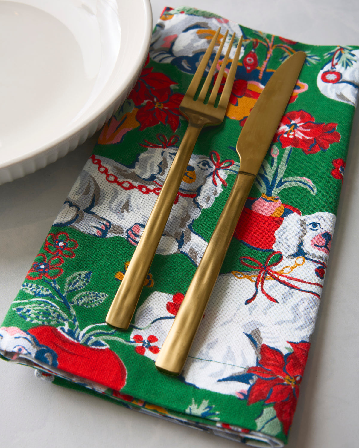 Close-up of a green Good Dog Christmas dinner napkin with a fork and knife resting on it beside a white bowl.