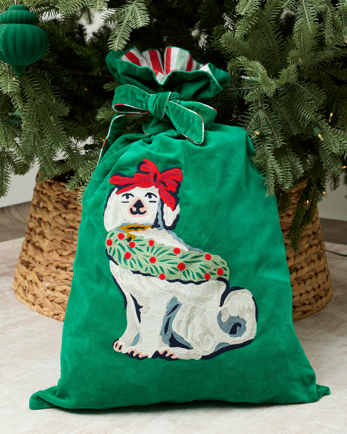 Green Good Dog Christmas gift sack with a bow-wearing white dog design, displayed beneath a Christmas tree