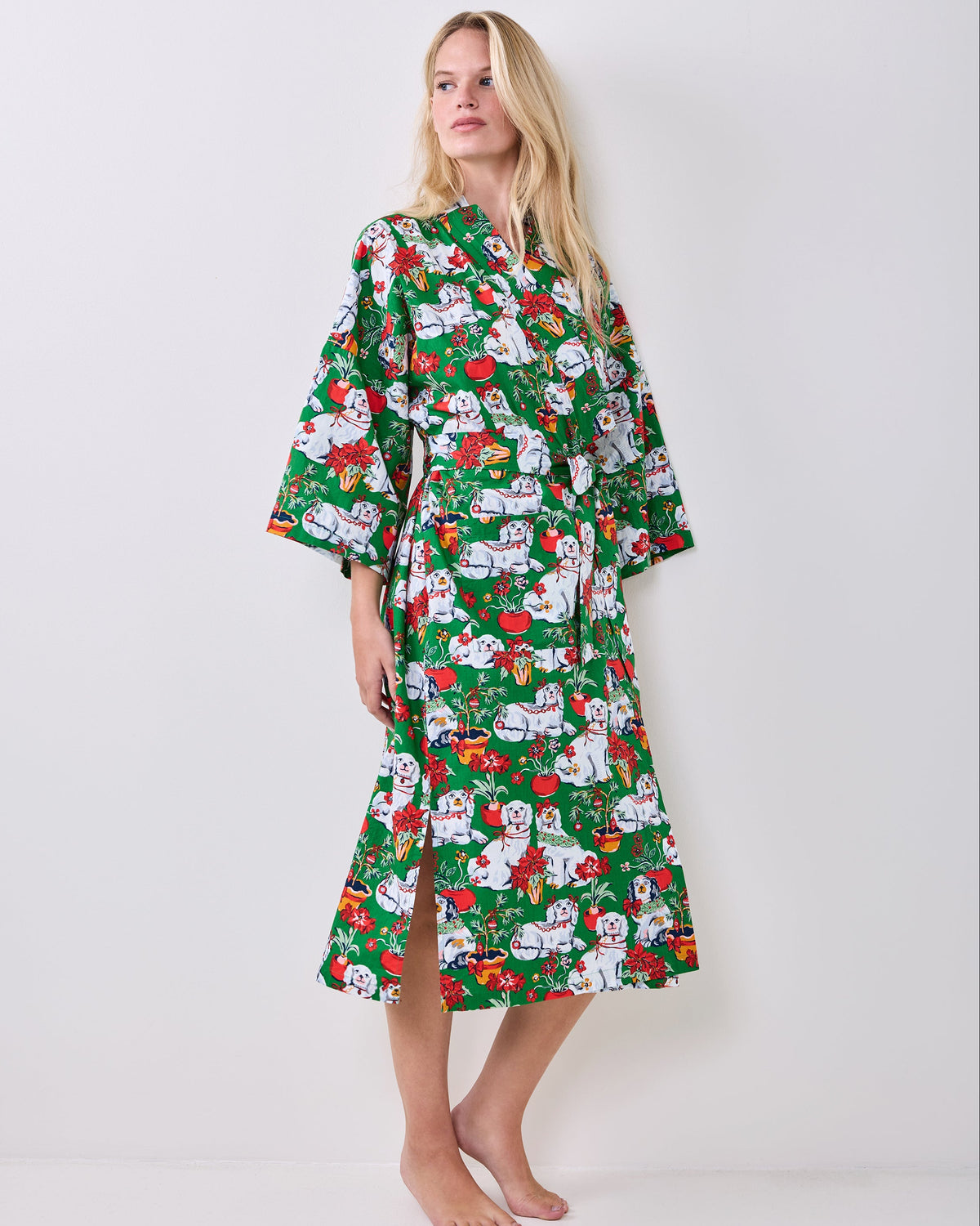 Full-length green Good Dog Christmas robe with wide sleeves, a tied belt, and a holiday print of white dogs, poinsettias, and Christmas decorations.