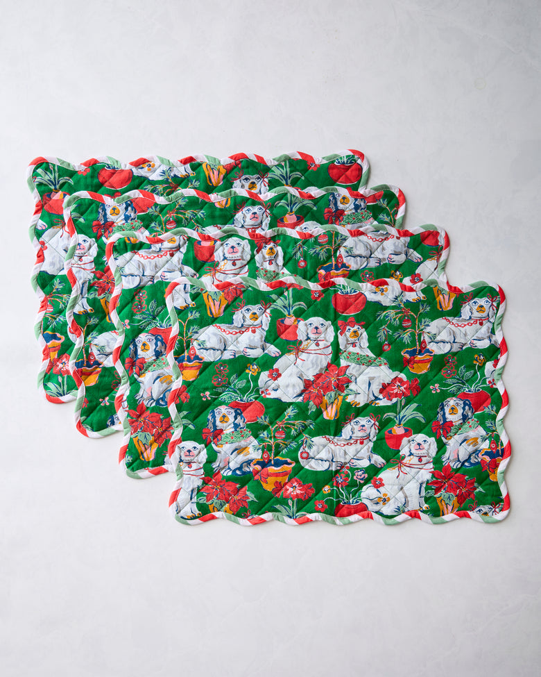 Four green Good Dog Christmas placemats overlapping in a staggered arrangement, showing scalloped edges and a dog-and-holiday print.