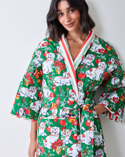 Front view of a person wearing a green reversible quilted robe patterned with Christmas dogs, flowers, and holiday motifs.