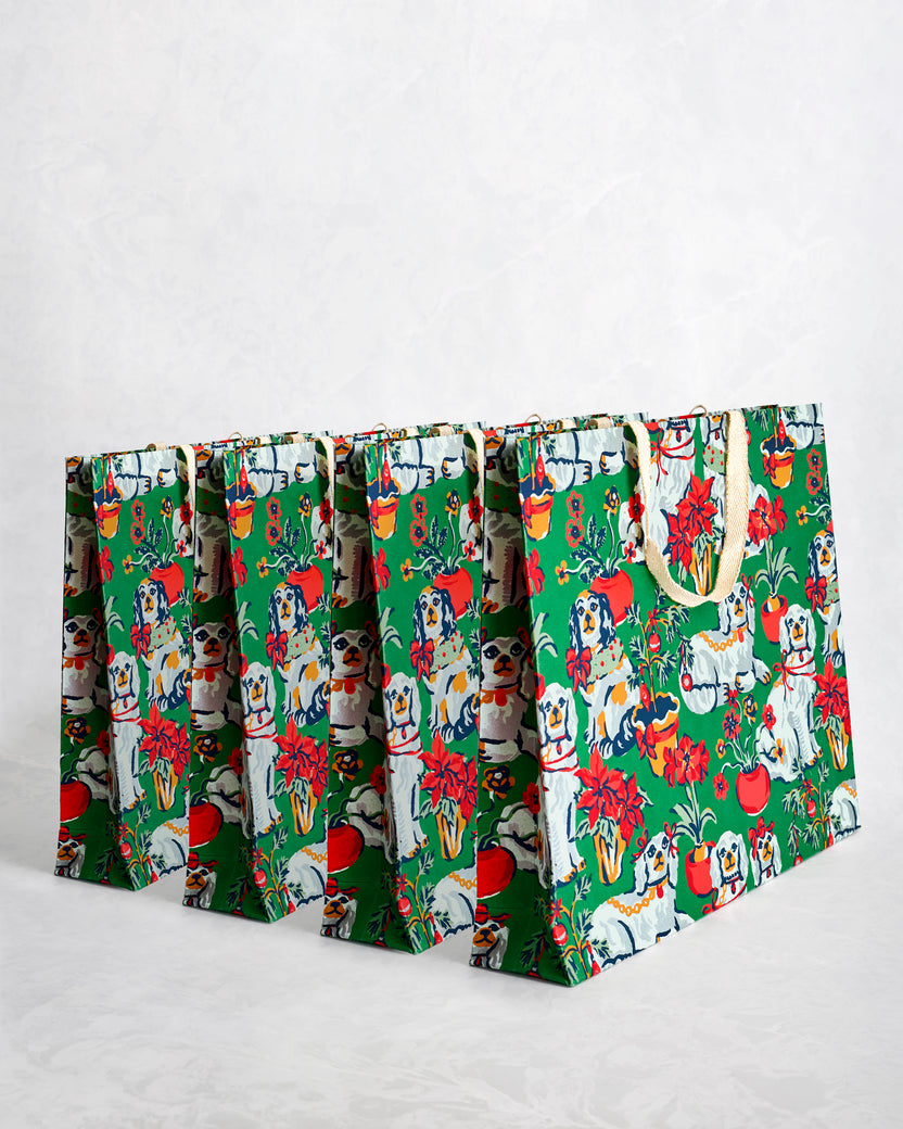 Set of four evergreen paper gift bags with illustrated dogs, flowers, and holiday motifs.