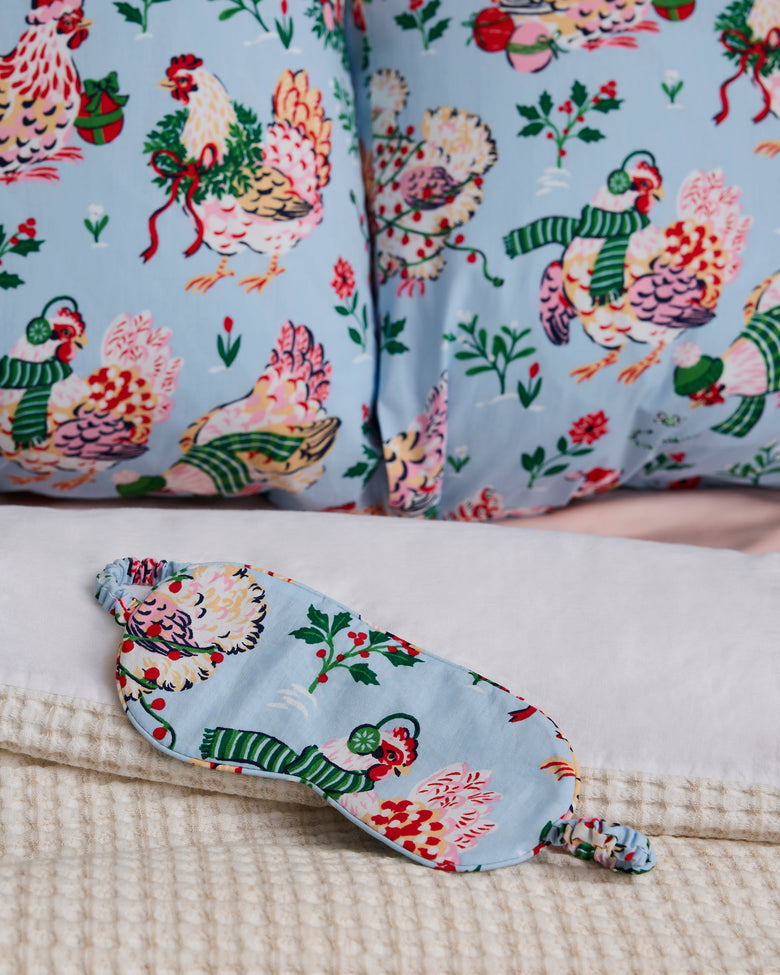 Close-up of the pale blue Holiday Hens pillowcase print with a matching sleep mask in the foreground.
