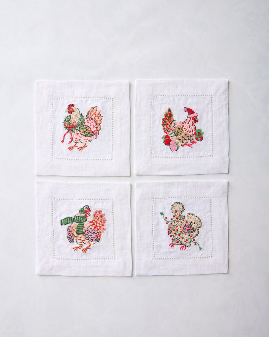 Set of four white cocktail napkins arranged in a square, each embroidered with a different holiday chicken