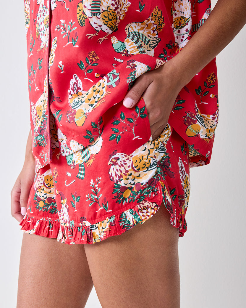 Close-up of the red Holiday Hens pajama shorts showing a side pocket, curved hem, ruffle trim, and chicken print.