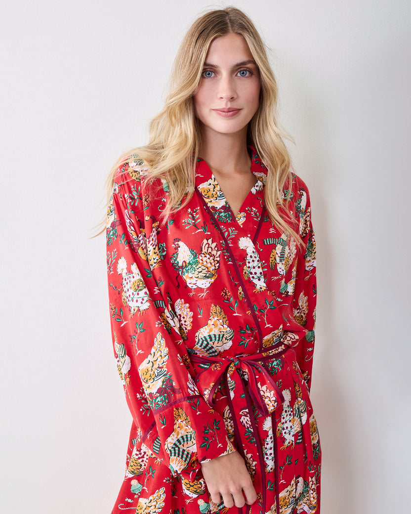 Person standing and wearing a red holiday hen-print robe with long sleeves and a waist tie.