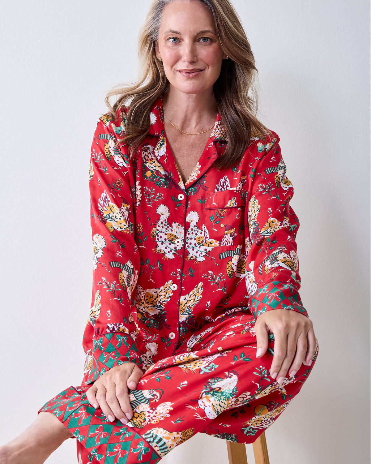 Close-up of the red Holiday Hens Soho pajama set with a collared button-front top, chest pocket, and matching pants printed with holiday hens and plants.
