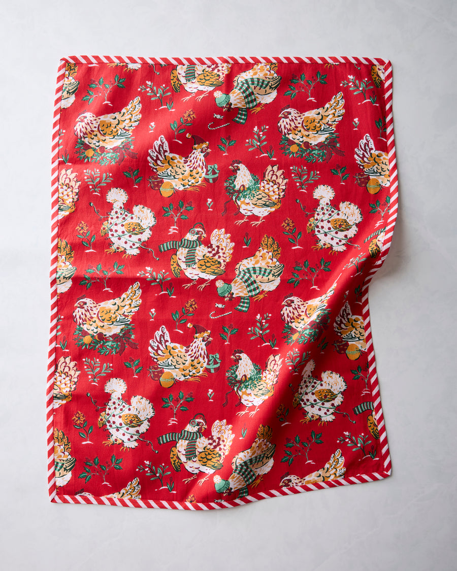 Red tea towel with a repeating illustrated holiday hen print and red-and-white striped edging, shown with one corner folded.