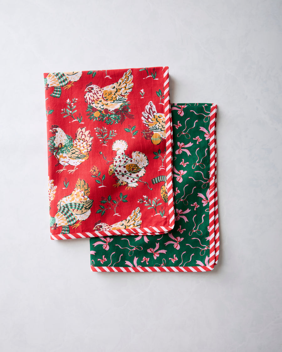 Two folded tea towels showing red holiday hen print and green pink-bow print, both with red-and-white striped edging.