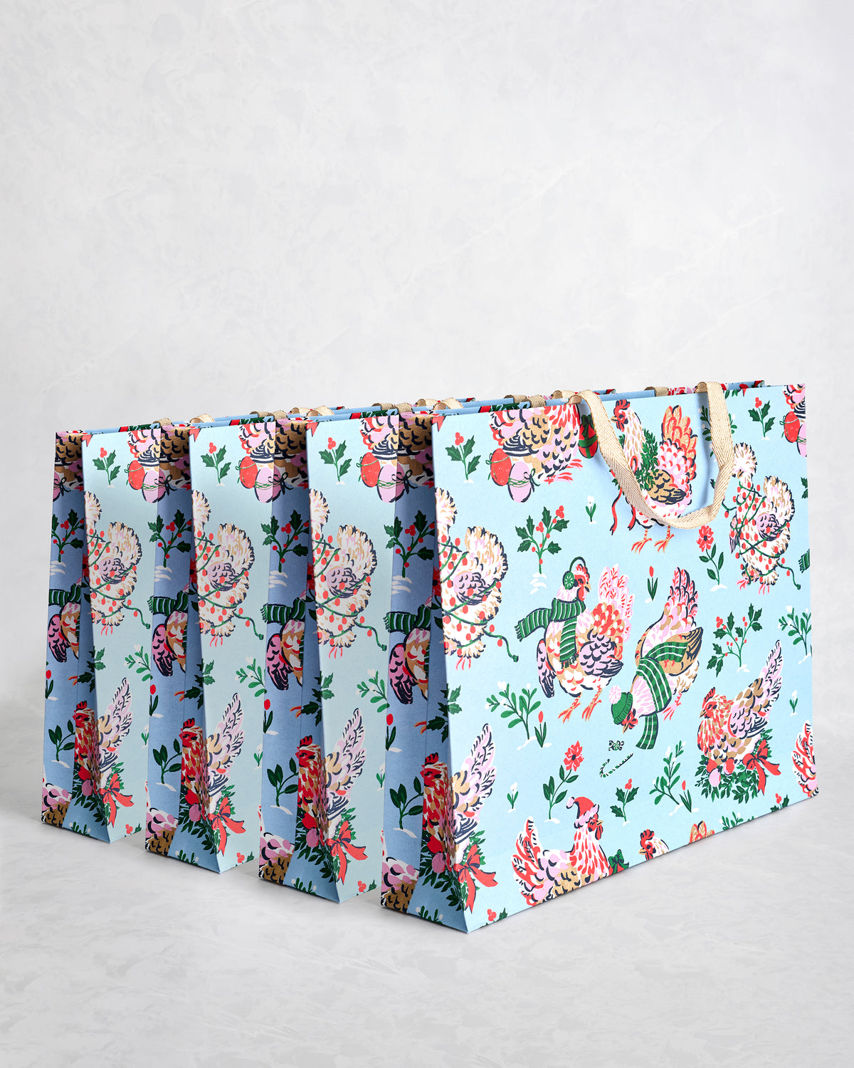 Set of four pale blue paper gift bags with holiday hen illustrations and sparkly handles.