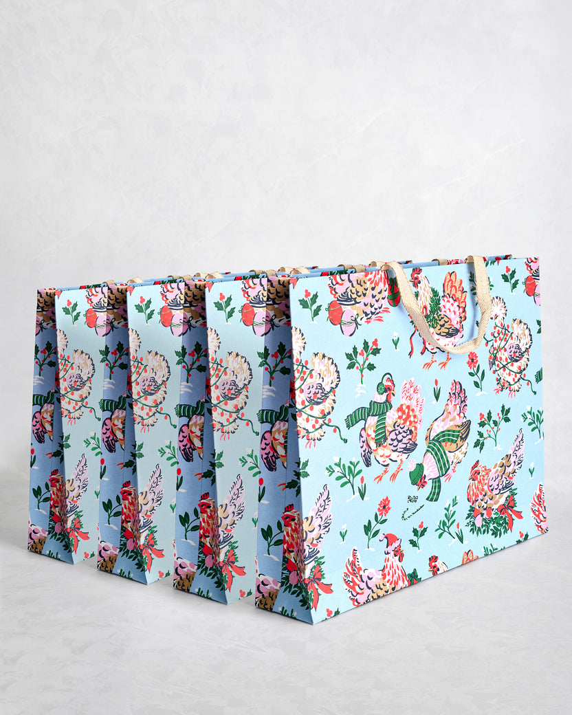 Set of four pale blue paper gift bags with holiday hen illustrations and sparkly handles.