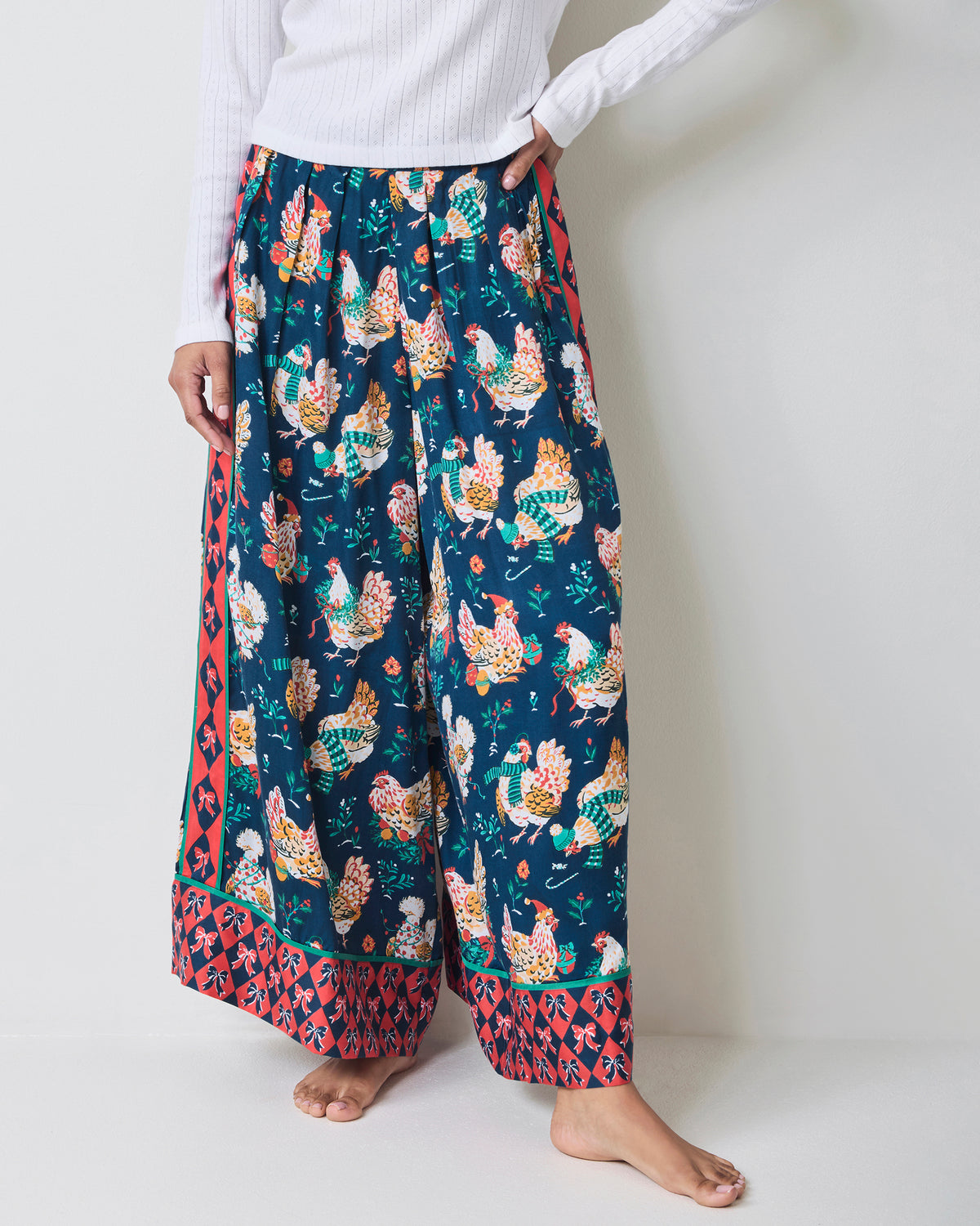 Model wearing navy chicken-print wide-leg pajama pants with a pull-on waist and contrasting patterned cuffs.