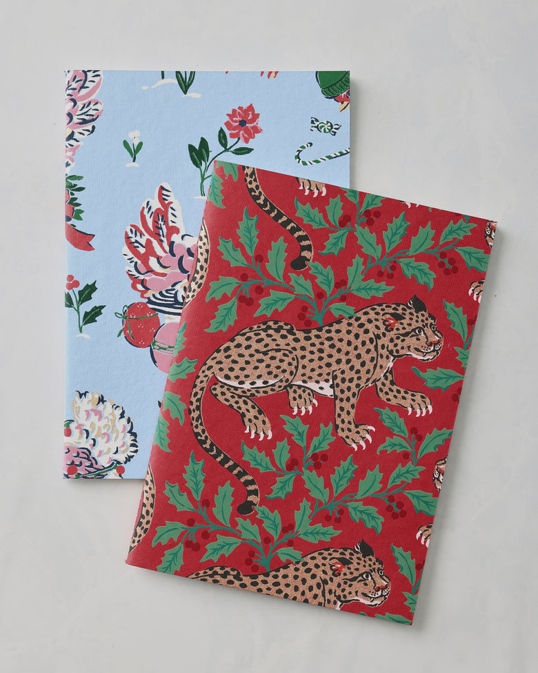 Red Holiday Icons notebook cover with spotted leopards and green holly foliage, overlapping a light blue patterned notebook.