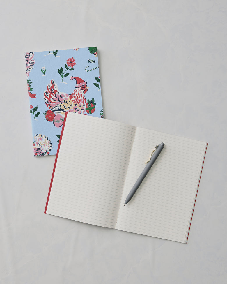 Open lined notebook with a gray pen, beside a closed floral bird-print notebook.