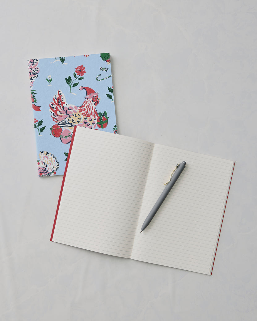 Open lined notebook with a gray pen, beside a closed floral bird-print notebook.
