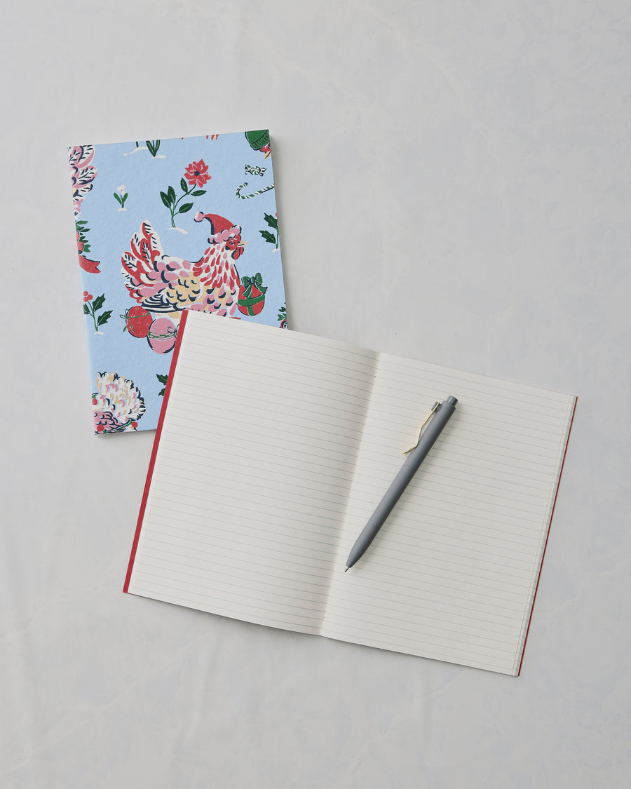 Open lined notebook with a gray pen, beside a closed floral bird-print notebook.
