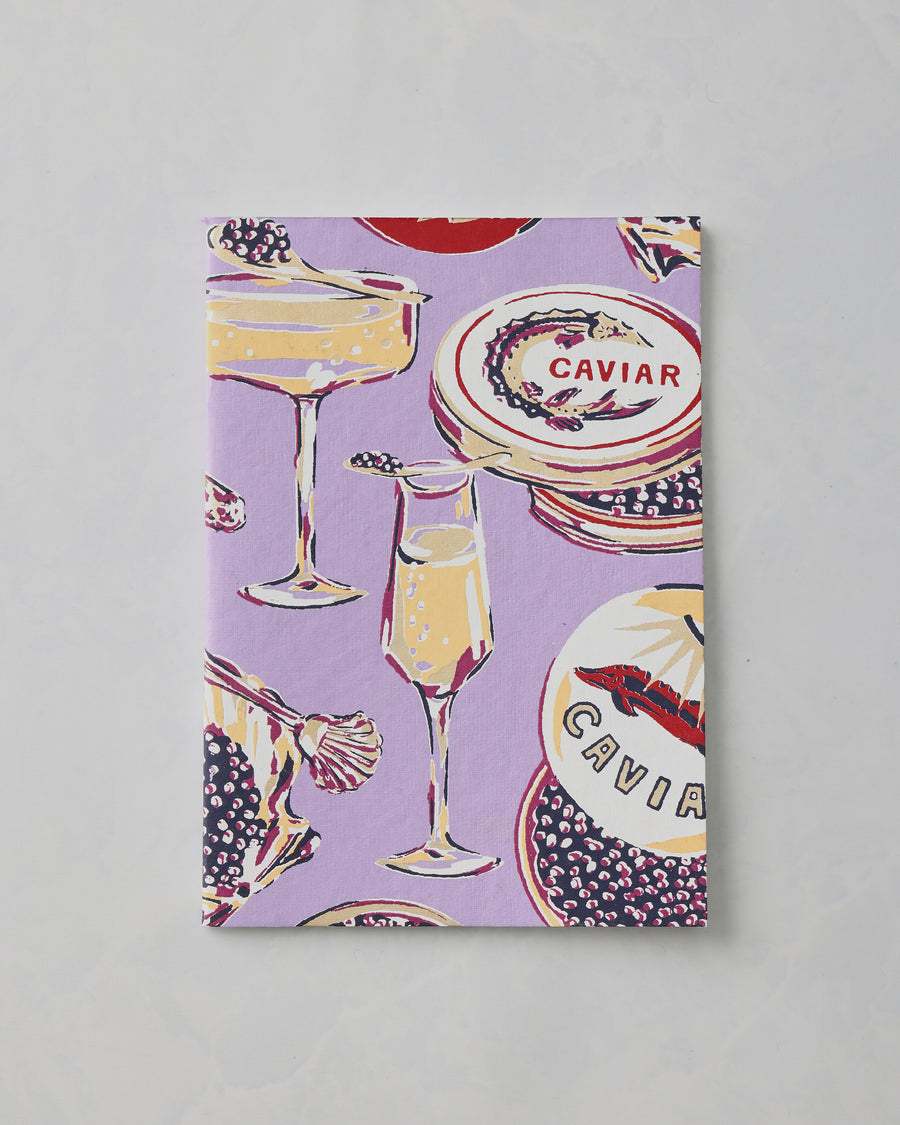 Lavender Champagne and Caviar notebook cover with illustrations of champagne glasses, caviar dishes, and the word “CAVIAR.”