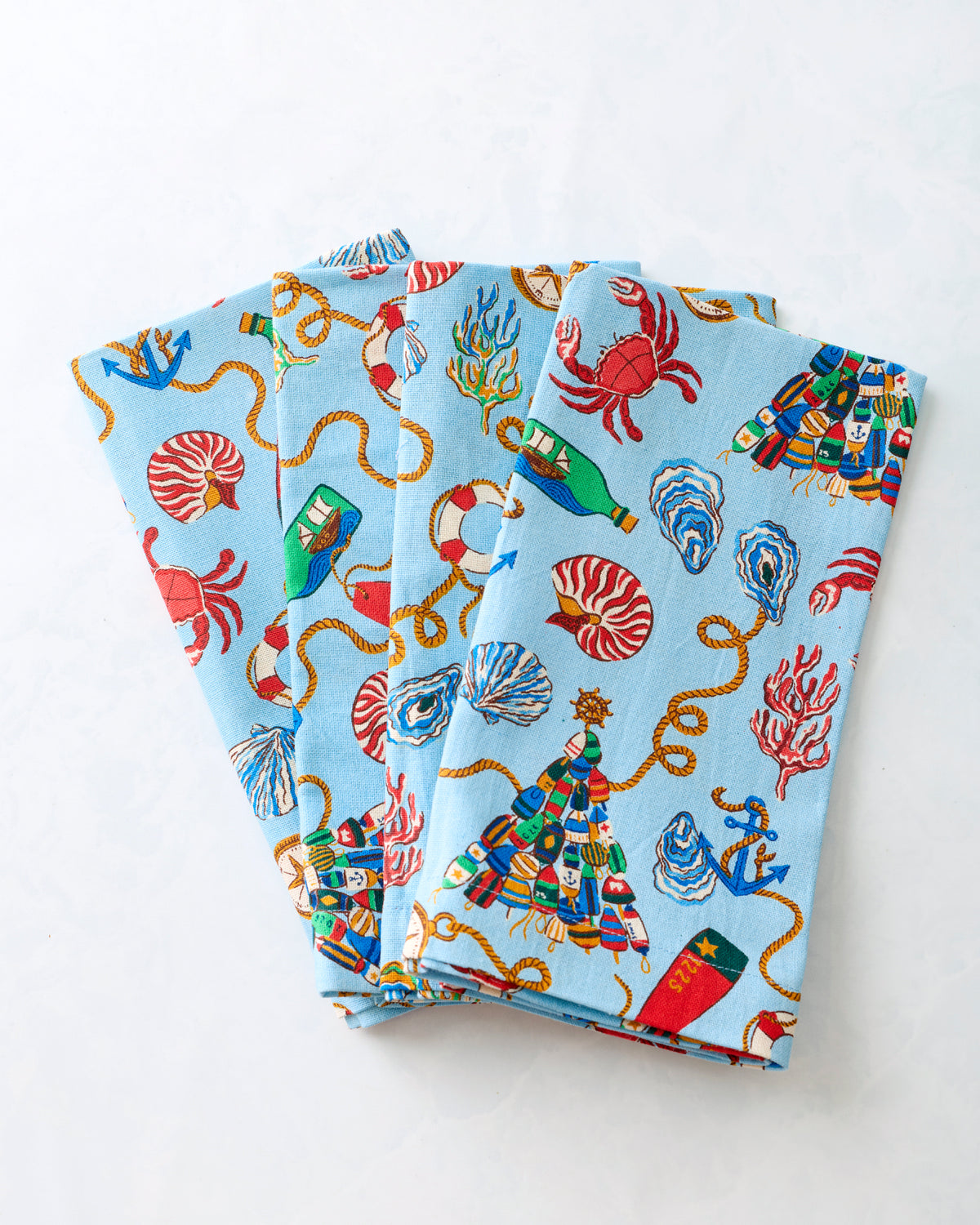 Four dinner napkins stacked and fanned out to show the repeating blue nautical Christmas print.