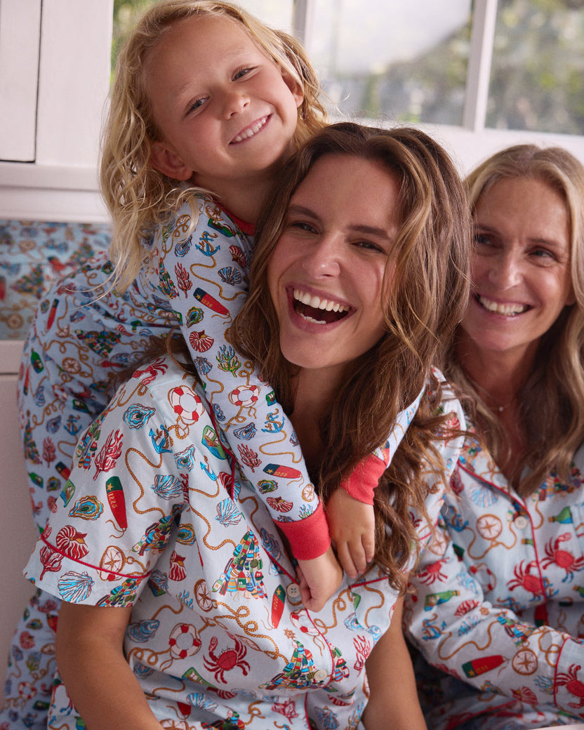 Child wearing a light blue nautical-print long-sleeve pajama set while being held by a person, with another person beside them.