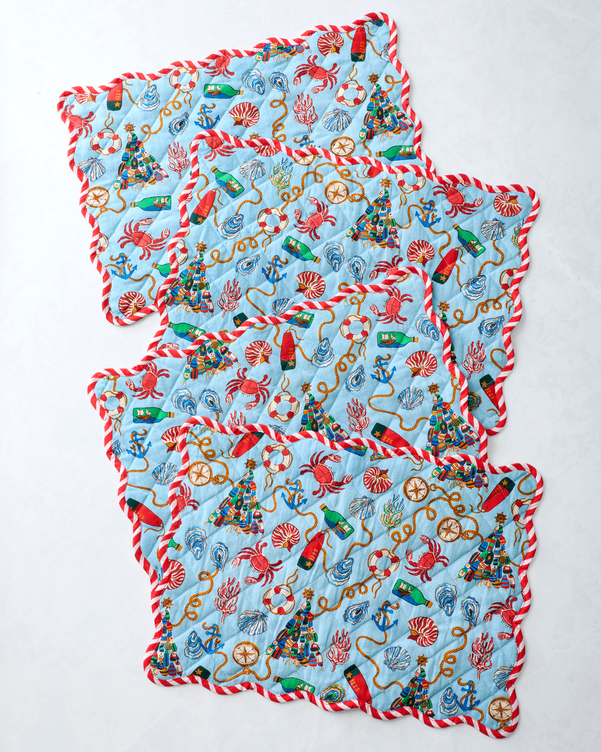 Four blue printed placemats overlapped to display the repeating nautical Christmas design and red-and-white trim.