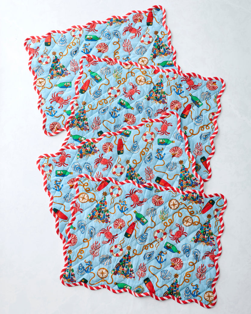 Four blue printed placemats overlapped to display the repeating nautical Christmas design and red-and-white trim.