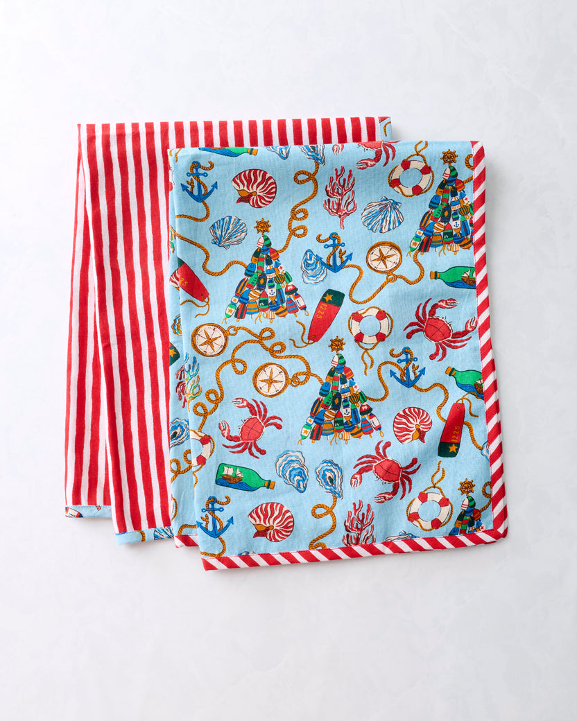Two tea towels layered to show the blue nautical Christmas print and red-and-white striped reverse.