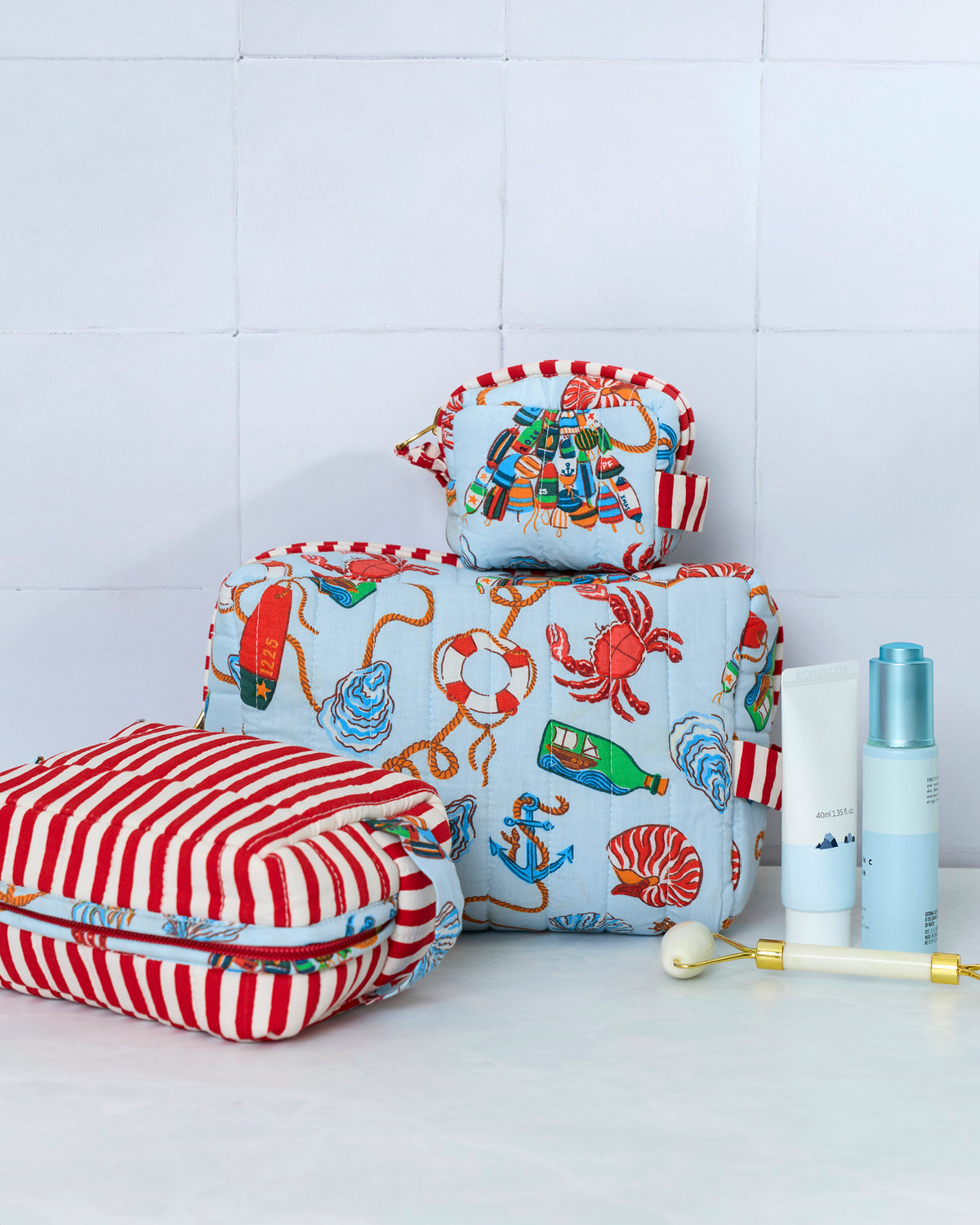 Three patterned pouches displayed with toiletries; a red-and-white striped pouch is in front of two pale blue nautical-print pouches.