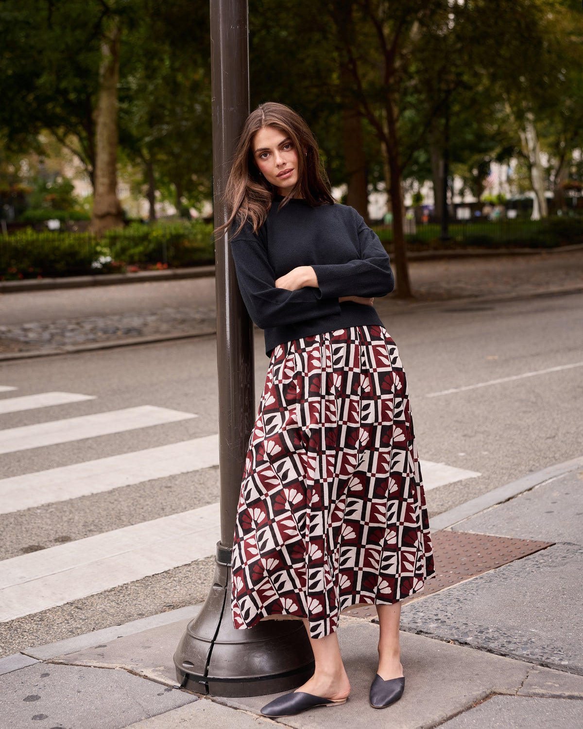 Person wearing the Hygge Greenhouse Sparrow Skirt with a dark long-sleeve top and black flats on a city street.