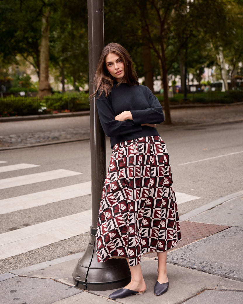 Person wearing the Hygge Greenhouse Sparrow Skirt with a dark long-sleeve top and black flats on a city street.