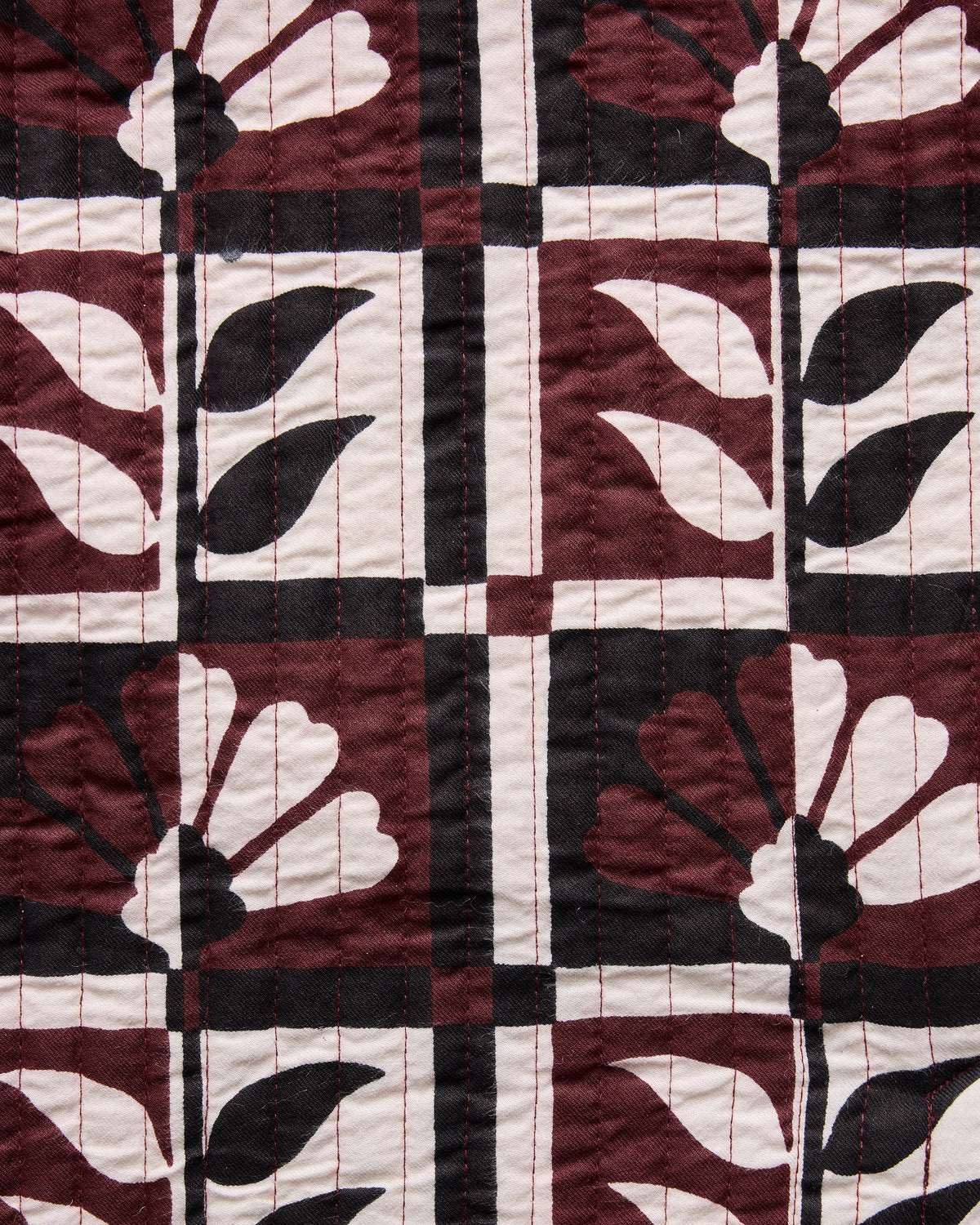 Close-up of the Hygge Greenhouse Bordeaux print showing stylized flowers and leaves in burgundy, cream, and dark brown geometric blocks.