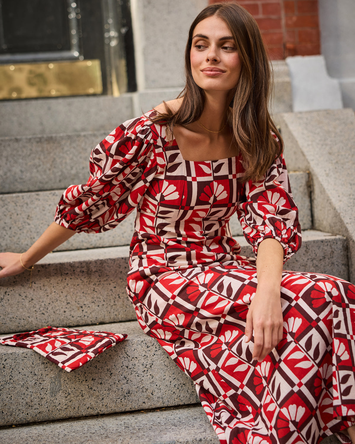 Seated front view of the Constance dress showing its square neckline, puff sleeves, and red-and-white floral geometric print.