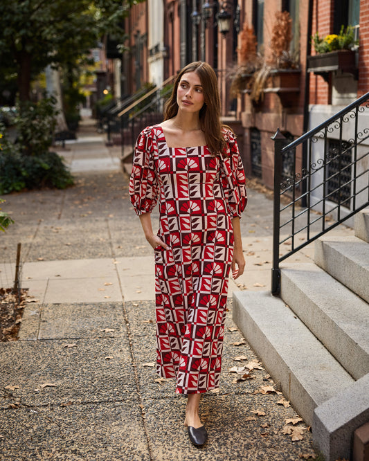 Person walking on a residential sidewalk wearing a red-and-cream geometric-patterned Constance dress with puff sleeves.