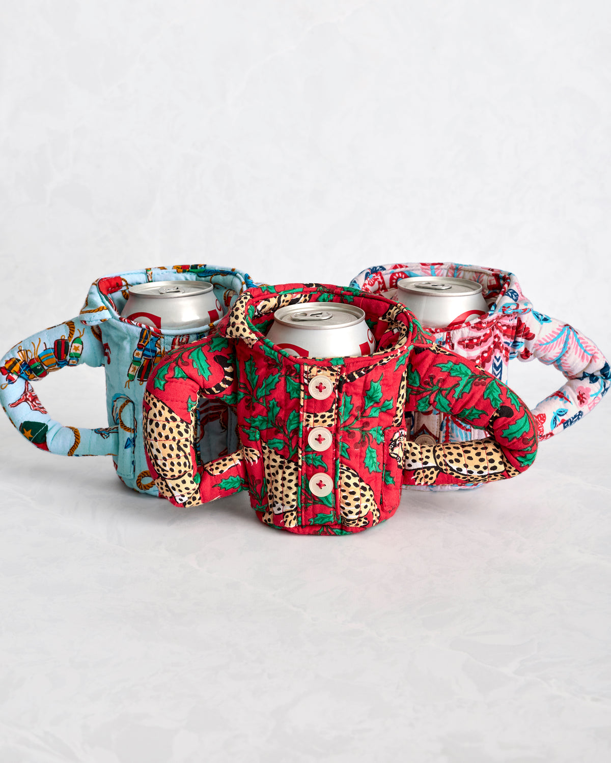 Three quilted can cozies with button fronts and handles in blue, red, and pink patterned prints