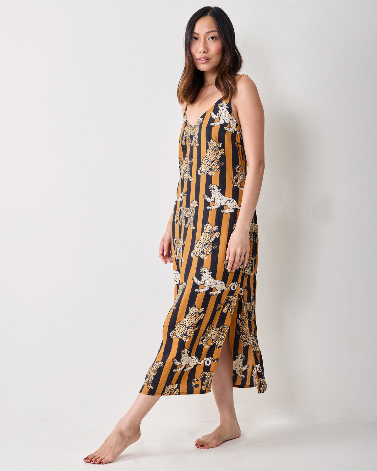 Full-length view of a person wearing a butterscotch-and-black striped midi nightie with leopard illustrations and a side slit.