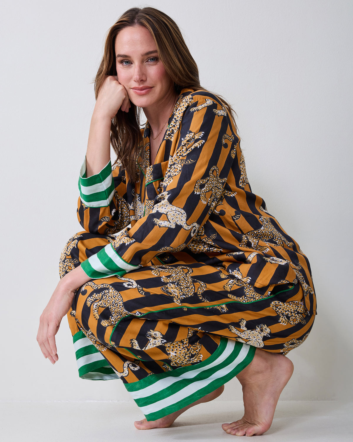 Person crouching while wearing a butterscotch-and-black striped Soho pajama set with leopard illustrations and green-and-white striped cuffs.
