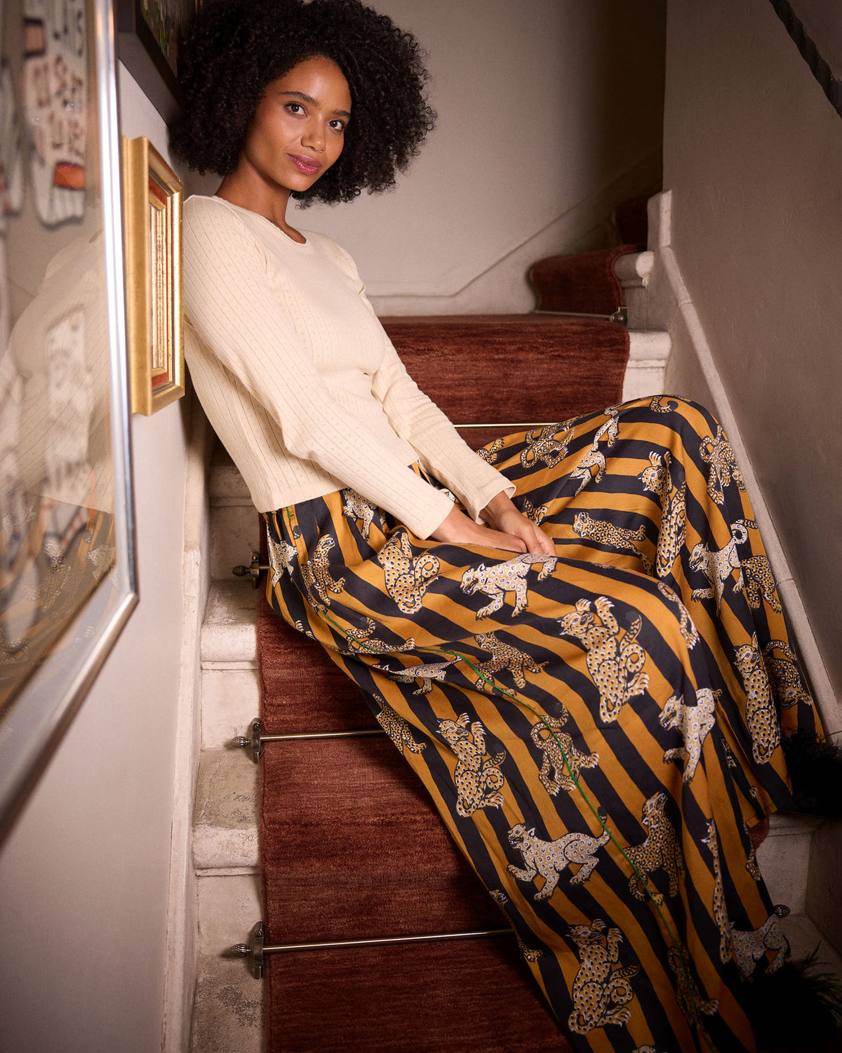 Side view of a model seated on stairs wearing the Leopard Stripes Tribeca pants, showing the wide-leg shape and mustard-and-black striped leopard print.