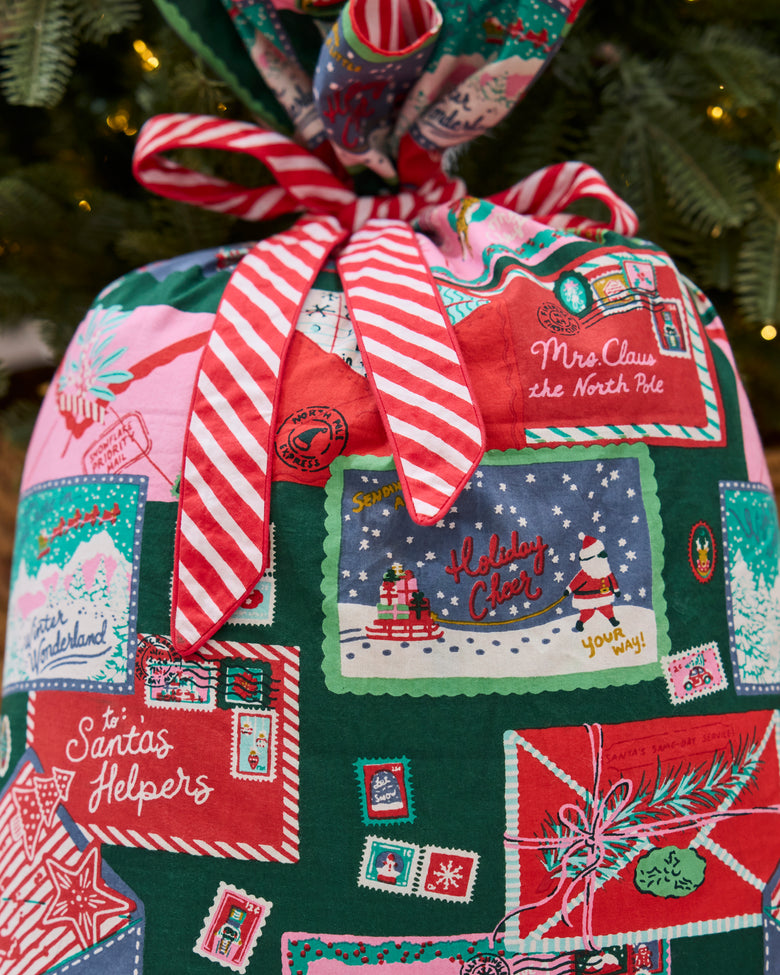 Close-up of the Christmas gift sack showing a red-and-white striped bow and illustrated holiday envelopes, stamps, and postage labels.