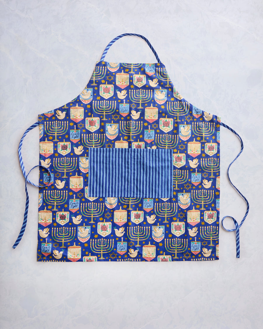 Flat view of a blue patterned apron with menorahs, stars, birds, and a large striped front pocket.