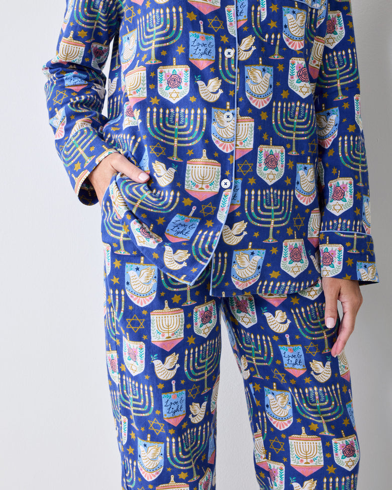 Close view of a blue long-sleeve pajama set with a Hanukkah print of menorahs, stars, dreidels, and other festive motifs.