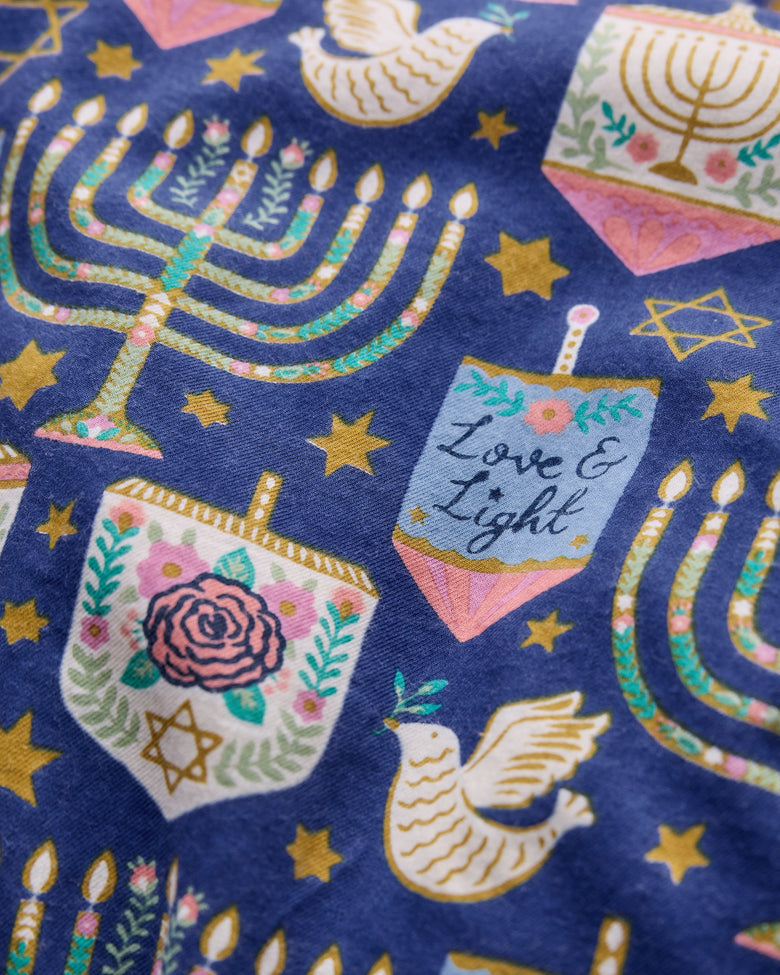 Close-up of the Hanukkah Blue Love & Light pants print with menorahs, stars, dreidels, roses, and doves on a dark blue background.